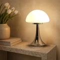 Lampe champignon Polka en verre opalin blanc allumée sur une console en pierre
