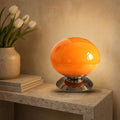 Lampe globe Opus en verre opalin orange allumée sur une console en pierre
