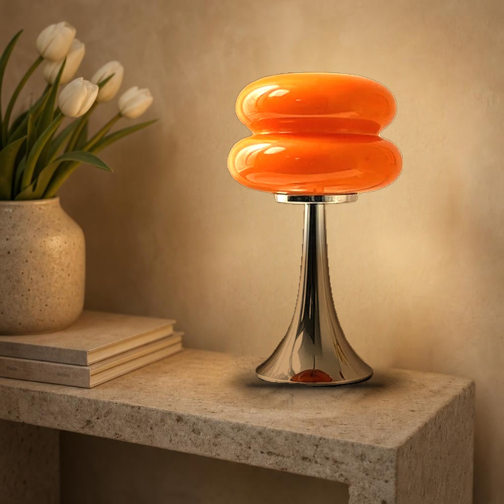 Lampe macaron Swing en verre orange allumée sur une console en pierre, pied tulipe chromé