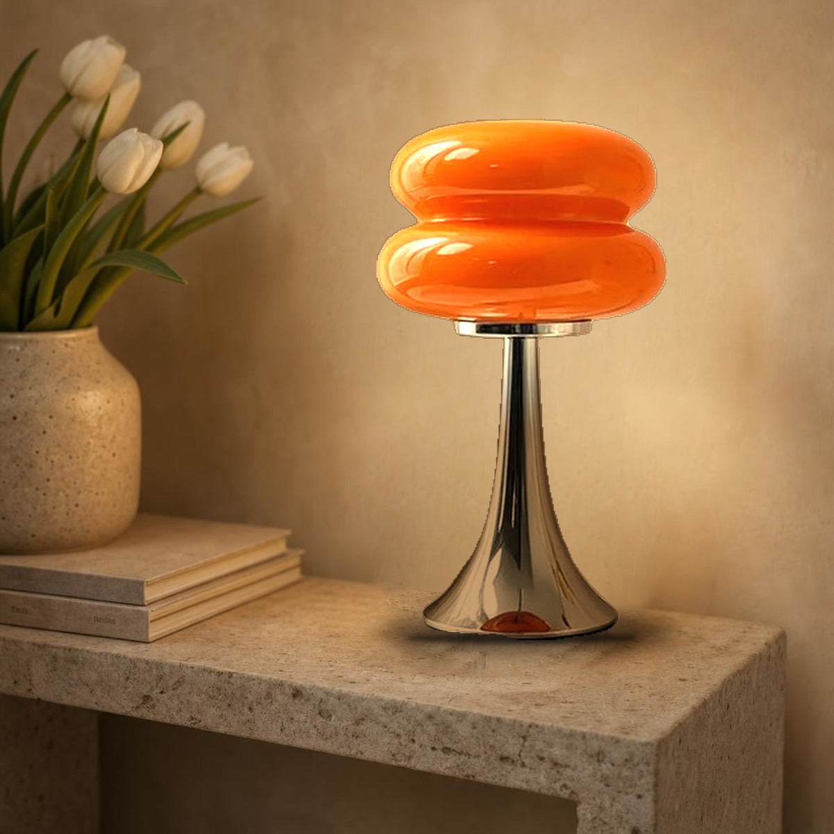 Lampe macaron Swing en verre orange allumée sur une console en pierre, pied tulipe chromé
