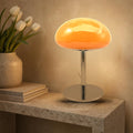 Lampe nuage Mazurka en verre opalin orange allumée sur une console en pierre