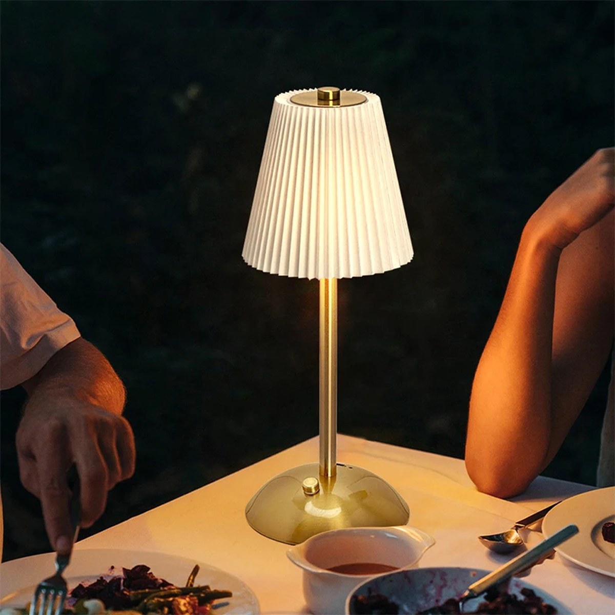Lampe sans fil Musette à abat-jour plissé blanc allumée sur une table de dîner