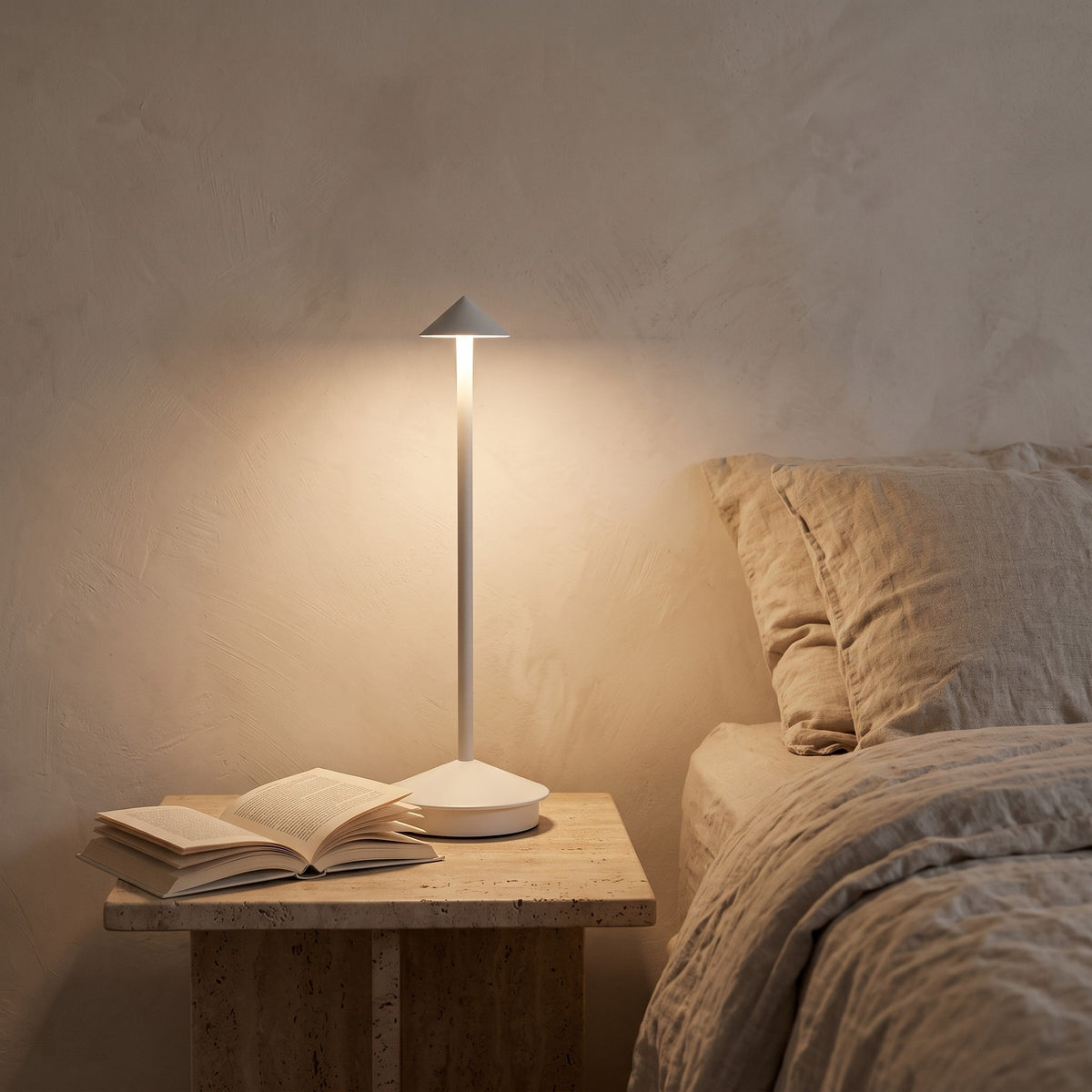 Lampe sans fil Solo blanche allumée sur une table de chevet en travertin